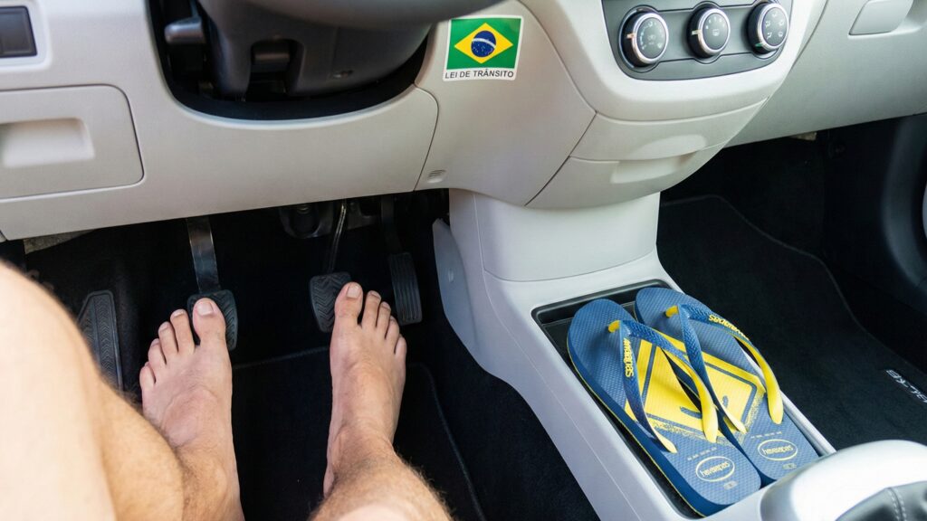 Homem dirigindo com os pés descalços e seu chinelo ao lado no carro