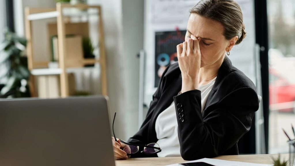 Trabalhador sentado em frente a tela de computador com expressão de cansaço e sobrecarga, representando sintomas de Burnout e esgotamento profissional no ambiente de trabalho.