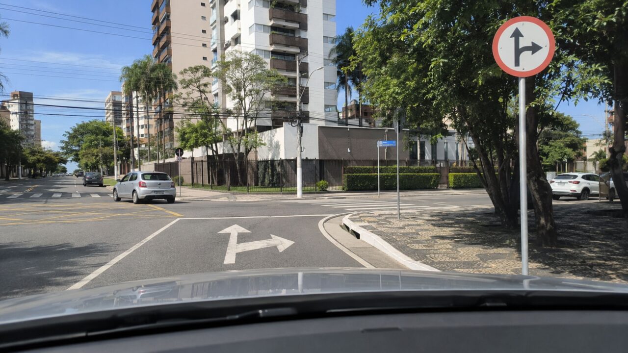 O que significa a placa de trânsito com borda vermelha, fundo branco e uma seta apontada para a direita?