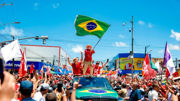 Lula com bandeira do brasil em cima de um carro durante comício